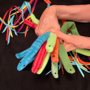 May include: A set of colorful plush worm toys with black eyes. The worms are made of soft, fuzzy fabric and are tied together with colorful ribbons.