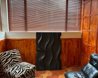 May include: A black 3D wall panel with a wavy design, mounted on a wall with wood paneling. The panel is in a room with two chairs, one with a zebra print and the other with black leather upholstery.