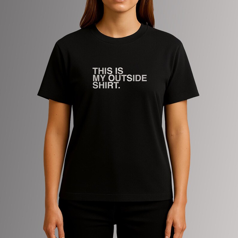 Puede incluir: Camiseta negra con el texto blanco "THIS IS MY OUTSIDE SHIRT." centrado en el pecho. La camiseta tiene mangas cortas y cuello redondo. La modelo lleva pantalones negros.