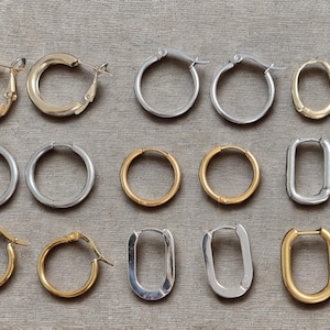 Peut inclure: Une collection de boucles d'oreilles créoles dorées et argentées de différentes formes et tailles. Les boucles d'oreilles comprennent des créoles rondes classiques, des créoles ovales et des créoles rectangulaires. Les boucles d'oreilles sont présentées sur une surface de ton neutre.