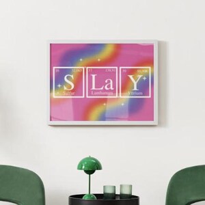 Puede incluir: Una impresión enmarcada con un fondo degradado rosa, amarillo, azul y morado. La impresión presenta la palabra "SLAY" deletreada usando los símbolos químicos del azufre, el lantano y el itrio.