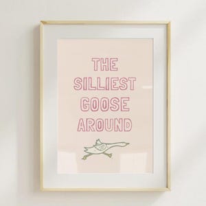Könnte beinhalten: Ein gerahmter Druck mit rosa Hintergrund und weißem Text, der "The Silliest Goose Around" lautet. Ein Cartoon-Gans läuft am unteren Rand des Drucks.