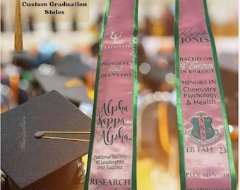 May include: Two pink and green graduation stoles with custom text. The left stole has the text "Lafayette", "Presidents and Dean's List", "Alpha Kappa Alpha", "National Society of Leadership and Success", and "Research Assistant". The right stole has the text "Kaya Jones", "Bachelor of Science in Biology", "Minors in Chemistry, Psychology & Health", "EB Fall '23", "Peer Mentor", and "Pre-Professional Society".