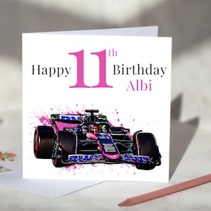 Puede incluir: Una tarjeta de cumpleaños blanca con el texto "Happy 11th Birthday Albi" en negro y rosa. La tarjeta presenta un diseño de coche de carreras rosa y negro con un fondo de salpicaduras de pintura rosa. Un lápiz rosa está en la esquina inferior derecha.