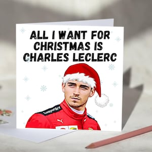 Könnte beinhalten: Eine Weihnachtskarte mit dem Text "ALL I WANT FOR CHRISTMAS IS CHARLES LECLERC". Die Karte zeigt eine Illustration von Charles Leclerc mit Weihnachtsmütze und rotem Rennanzug. Schneeflocken sind auf dem weißen Hintergrund verstreut.