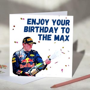 以下が含まれることがあります： 「ENJOY YOUR BIRTHDAY TO THE MAX」と青色で書かれたバースデーカード。レッドブルのレーシングユニフォームを着た人物がシャンパンのボトルを開け、紙吹雪が舞うイラストが描かれています。