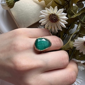 Puede incluir: Un anillo de oro con una gran piedra preciosa verde facetada. La piedra preciosa tiene un patrón estriado.