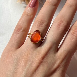 Può includere: Un anello d'oro con una grande pietra arancione a forma di lacrima.