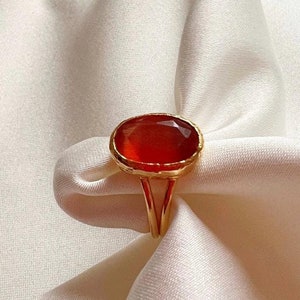 Può includere: Un anello d'oro con una grande pietra rossa di forma ovale.