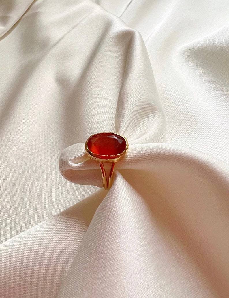 May include: A gold ring with a large, oval-shaped, red gemstone.
