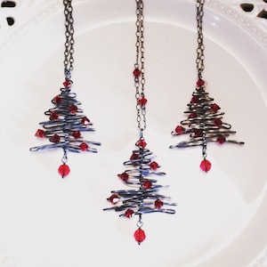 May include: Three silver wire Christmas tree necklaces with red crystal ornaments.
