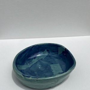 Puede incluir: Un pequeño cuenco de cerámica de forma ovalada con un esmalte azul y verde. El cuenco tiene una superficie ligeramente texturizada y un interior profundo y redondeado.
