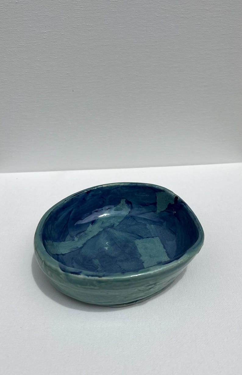 Peut inclure: Un petit bol en c&eacute;ramique de forme ovale avec un gla&ccedil;age bleu et vert. Le bol a une surface l&eacute;g&egrave;rement textur&eacute;e et un int&eacute;rieur profond et arrondi.