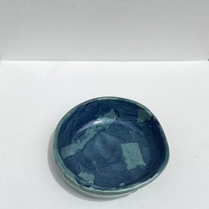 Peut inclure: Un petit bol rond en c&eacute;ramique avec un gla&ccedil;age bleu et vert. Le bol a une forme irr&eacute;guli&egrave;re et un bord l&eacute;g&egrave;rement in&eacute;gal.