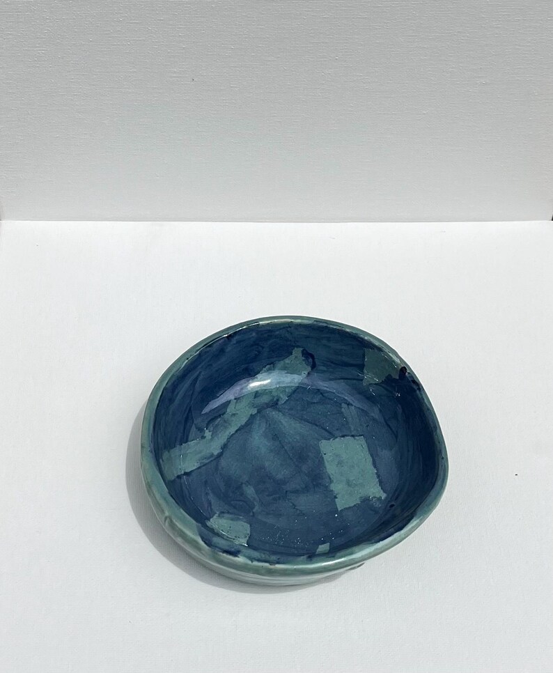 Peut inclure: Un petit bol rond en c&eacute;ramique avec un gla&ccedil;age bleu et vert. Le bol a une forme irr&eacute;guli&egrave;re et un bord l&eacute;g&egrave;rement in&eacute;gal.