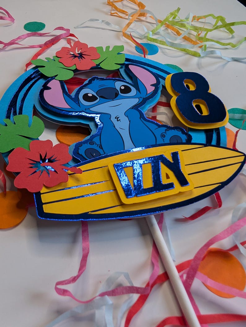 May include: Blue Stitch character sitting on a yellow surfboard with a blue "8th Day" banner. The character is surrounded by green leaves and red flowers.