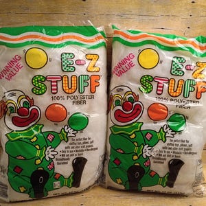 May include: Two clear plastic bags of E-Z Stuff 100% polyester fiberfill. Each bag features a colorful clown graphic juggling balls, with the text Winning Value, E-Z Stuff, and 100% Polyester Fiber printed on the front of the packaging.