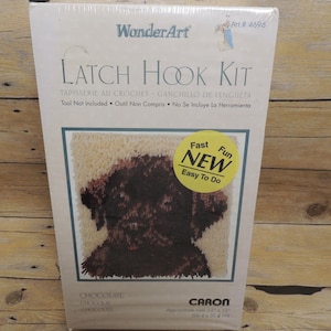 May include: A WonderArt Latch Hook Kit in a white box featuring a chocolate-colored puppy graphic. The packaging includes the text WonderArt, Latch Hook Kit, Art. #4696, and a yellow circular sticker that reads Fast Fun NEW Easy To Do.