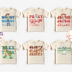 Puede incluir: Seis camisetas de color crema con personajes de una popular película de animación. Cada camiseta tiene un diseño de personaje diferente con el nombre del personaje impreso en una fuente colorida. Los personajes incluyen a Woody, Forky, Jessie, Rex, Slinky y Buzz Lightyear.