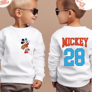 Könnte beinhalten: Zwei weiße Sweatshirts mit einem Mickey Mouse Design. Ein Sweatshirt zeigt Mickey Mouse beim Baseballspielen, das andere hat den Text "MICKEY 28" auf der Rückseite.