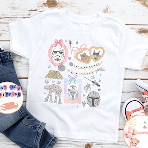 May include: White t-shirt with Star Wars illustrations, including a Stormtrooper and R2-D2, and the phrase "May the Force Be With You." The design is paired with blue jeans and pink trainers.