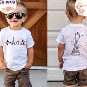 May include: White t-shirt with a black and white Eiffel Tower graphic on the back and a Mickey Mouse and Minnie Mouse graphic with the word "PARIS" on the front. The shirt is being worn by a young child.