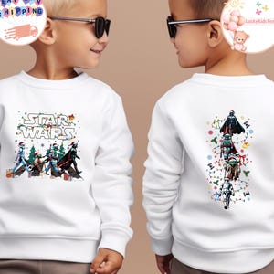 May include: White sweatshirt with a Star Wars design, featuring characters in festive attire. The front shows the Star Wars logo and characters. The back displays characters in a vertical line with Christmas lights and snowflakes.