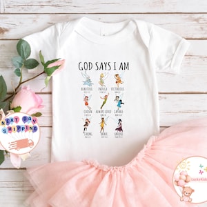 May include: White baby onesie with a pink tulle skirt. The onesie has a graphic of Tinkerbell characters with the text "God Says I Am" and a list of positive affirmations with bible verses.