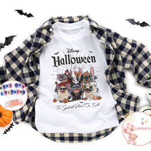 May include: White t-shirt with a Disney Halloween graphic featuring Stitch and friends in Halloween costumes. The shirt is layered under a blue and black plaid flannel shirt. Decorative bats and a pumpkin are also present.