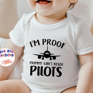 Può includere: Un body per neonati bianco a maniche corte con una grafica nera di un aereo al centro. Il testo stampato in nero recita I'M PROOF MOMMY CAN'T RESIST PILOTS, con l'icona dell'aereo posizionata tra la prima e la seconda riga di testo.