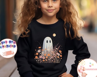 May include: Black sweatshirt featuring a white ghost design surrounded by colorful flowers and a full moon. The ghost has two oval eyes and a simple mouth. The sweatshirt is worn by a young girl.