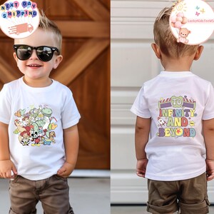 May include: A white t-shirt featuring a colorful graphic of cartoon characters, including a dinosaur, cowboy, and mouse. The back of the shirt has the text "TO INFINITY AND BEYOND" in a playful font. The child is wearing brown shorts and sunglasses.