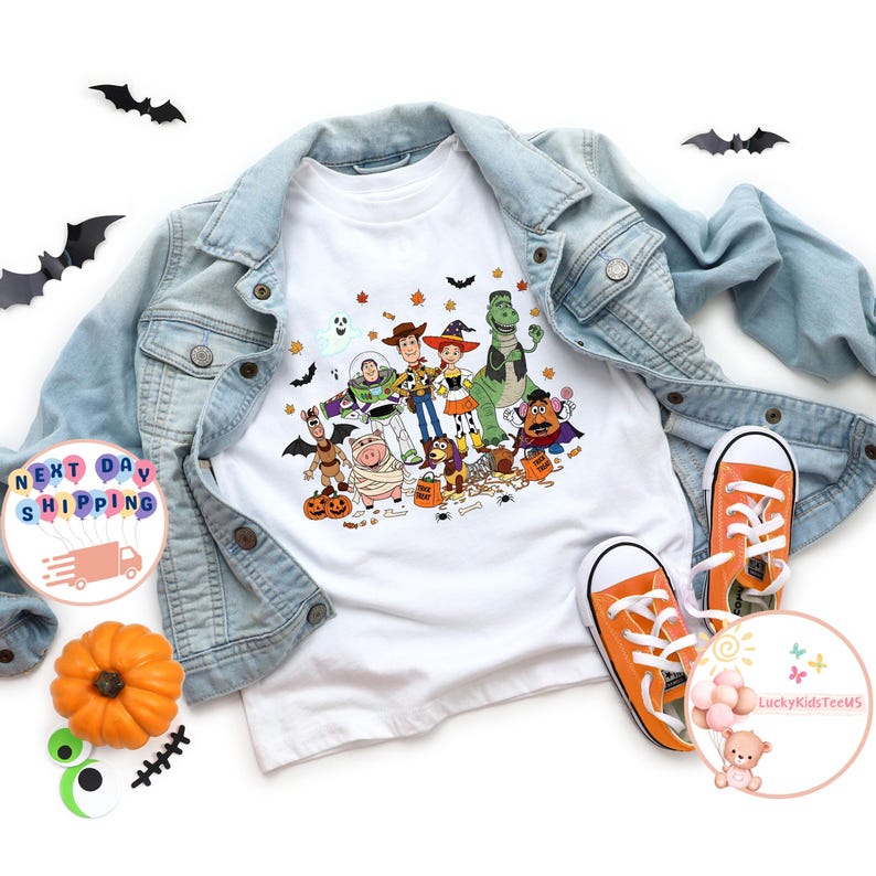 Puede incluir: Camiseta blanca con un colorido dise&ntilde;o de Halloween con personajes de Toy Story. La camiseta se combina con una chaqueta vaquera azul claro y zapatillas deportivas naranjas. Tambi&eacute;n hay murci&eacute;lagos decorativos y una calabaza.