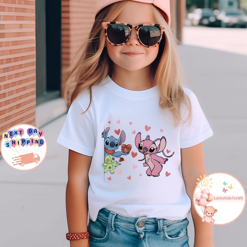 May include: White t-shirt featuring a cartoon graphic of Stitch and Angel with hearts. The design includes a blue Stitch holding a rose and a pink Angel holding a heart-shaped box. The shirt is worn by a child.