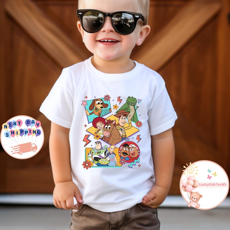 Op de afbeelding: Wit T-shirt met een kleurrijke afbeelding van personages uit de Toy Story-filmfranchise. De personages zijn Woody, Buzz Lightyear, Jessie, Rex en Mr. en Mrs. Potato Head.
