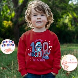 May include: Red sweatshirt with a blue cartoon character and the text "Happy 100th day of school" on the front.