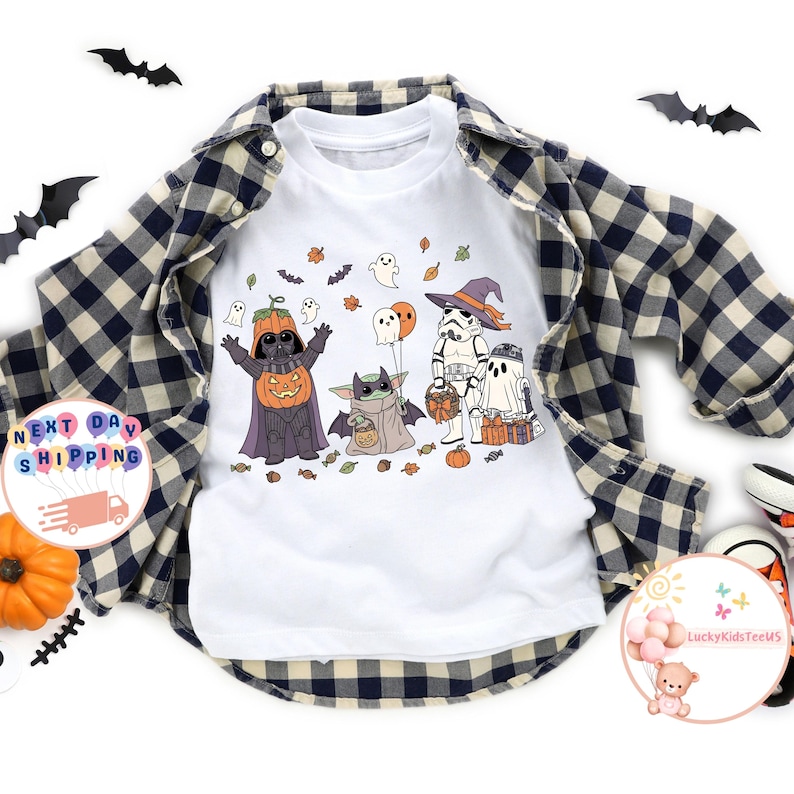 以下が含まれることがあります： ハロウィーンをテーマにしたグラフィックデザインの白いラグランスタイルのシャツ。デザインには、カボチャ姿のダース・ベイダー、ベビーヨーダ、ストームトルーパー、幽霊がすべてコスチュームを着ています。シャツは青と黒のチェック柄のシャツで重ね着されています。