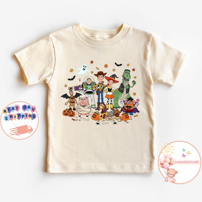 Puede incluir: Una camiseta color crema con un gr&aacute;fico colorido con tem&aacute;tica de Halloween de los personajes de Toy Story. El dise&ntilde;o incluye a Woody, Buzz Lightyear y otros personajes disfrazados, con murci&eacute;lagos, hojas y calabazas. La camiseta es de manga corta.