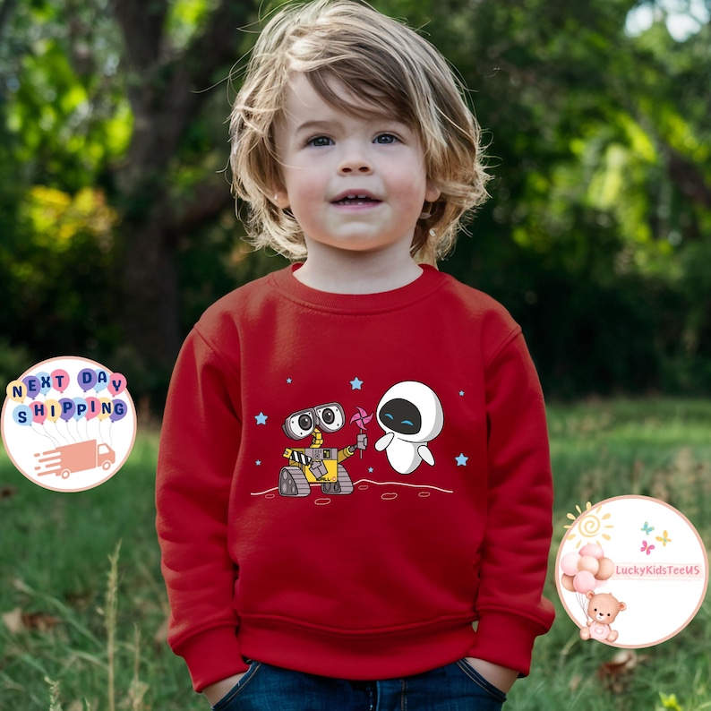 Puede incluir: Sudadera roja con una imagen de dibujos animados de Wall-E y Eve de la pel&iacute;cula Wall-E. Los personajes est&aacute;n de pie en un planeta con estrellas en el fondo.