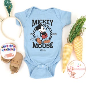 K&ouml;nnte beinhalten: Ein hellblauer Baby-Strampler mit einem Vintage-Mickey-Mouse-Motiv. Das Motiv zeigt Mickey Mouse in seiner charakteristischen roten Hose und gelben Schuhen. Der Text "Mickey Mouse" ist in einer schwarzen, abgenutzten Schriftart gedruckt, mit den Jahren "19" und "28" auf beiden Seiten des Motivs. Der Text "Disney" ist in einer kleineren Schriftart unter dem Motiv gedruckt.