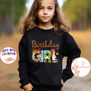 Op de afbeelding: Zwart sweatshirt met een afbeelding van Toy Story-personages die "Birthday Girl" spellen.