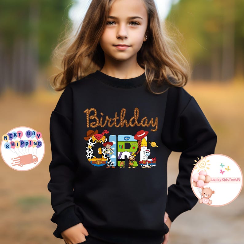 Op de afbeelding: Zwart sweatshirt met een afbeelding van Toy Story-personages die "Birthday Girl" spellen.