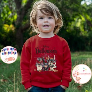 May include: A red sweatshirt featuring a Disney Halloween design. The graphic includes Stitch characters dressed in Halloween costumes, with the words "Disney Halloween" above. The design is centered on the front of the sweatshirt.