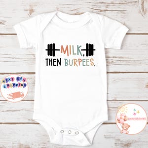 May include: White baby bodysuit with the text "MILK, THEN BURPEES" in black, orange, and blue lettering. The design includes a barbell graphic. A cute and funny outfit for a baby.