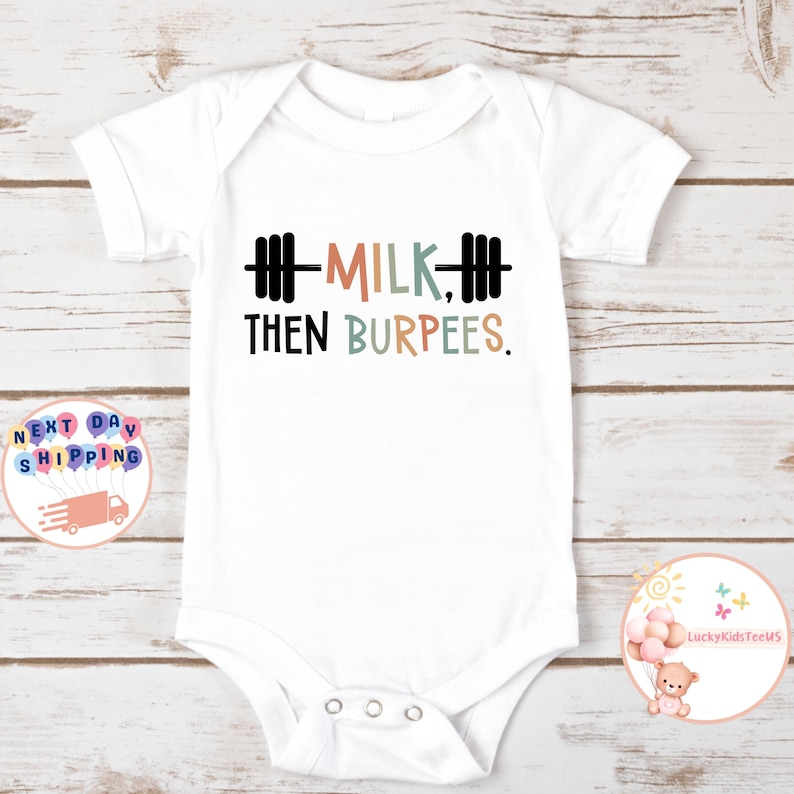 May include: White baby bodysuit with the text "MILK, THEN BURPEES" in black, orange, and blue lettering. The design includes a barbell graphic. A cute and funny outfit for a baby.