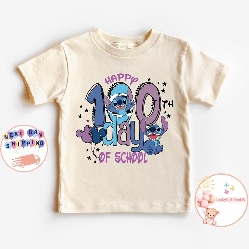May include: A light beige t-shirt with a blue and purple graphic of Stitch characters celebrating the 100th day of school. The text "Happy 100th day of school" is printed on the shirt.