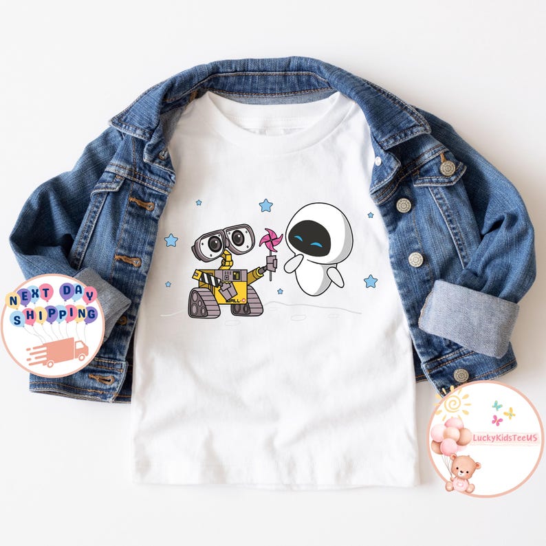 Puede incluir: Camiseta blanca con una imagen de dibujos animados de Wall-E y Eve de la pel&iacute;cula Wall-E. Wall-E sostiene una veleta rosa y Eve sonr&iacute;e.