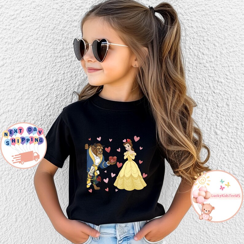 May include: Black t-shirt featuring a cartoon illustration of Belle and the Beast with heart accents. Belle is wearing a yellow dress, and the Beast is in a blue coat. The shirt is worn by a young person.
