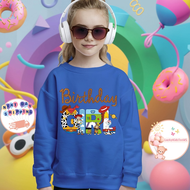 Op de afbeelding: Een koninklijk blauw sweatshirt met een afbeelding van de Toy Story-personages die "Birthday Girl" spellen.