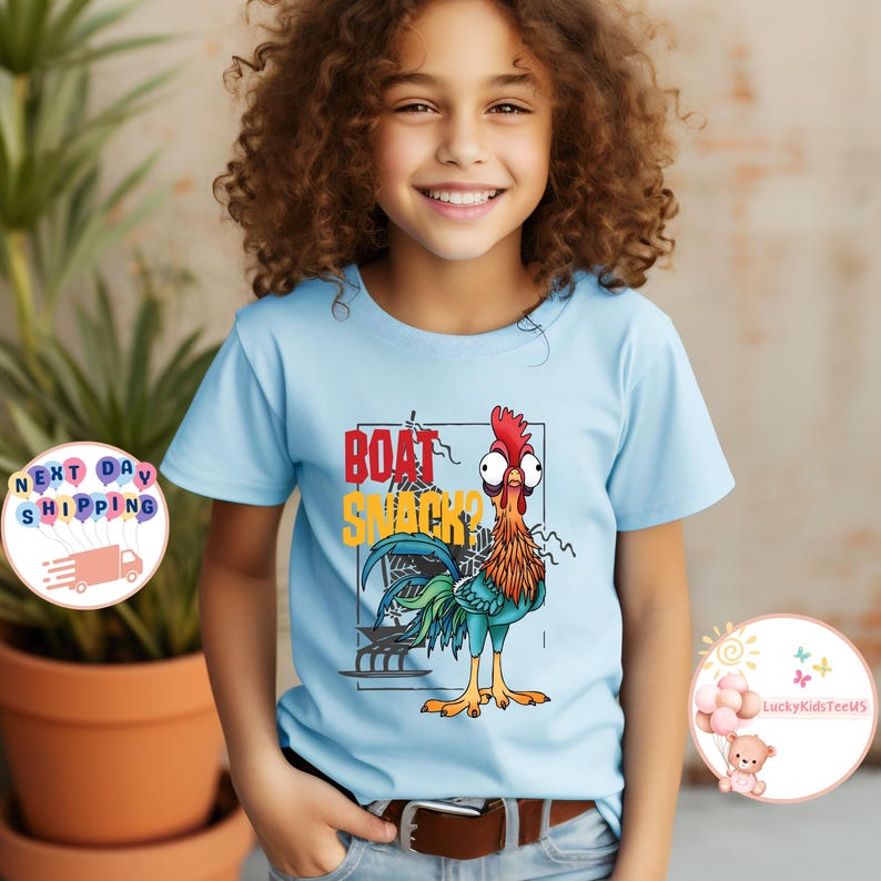 Peut inclure: T-shirt bleu clair avec un coq de dessin anim&eacute; et l'inscription "BOAT SNACKS?" en rouge et jaune. Le coq a une cr&ecirc;te rouge, des plumes orange et bleues et de grands yeux. Le t-shirt est port&eacute; par un enfant.